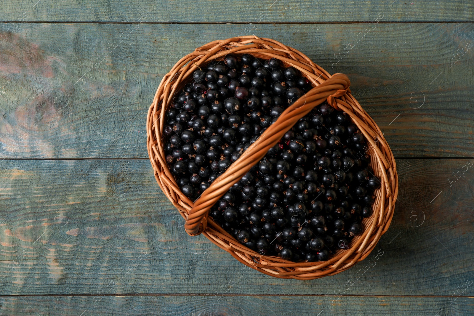 Photo of Ripe blackcurrants in wicker basket on wooden rustic table, top view