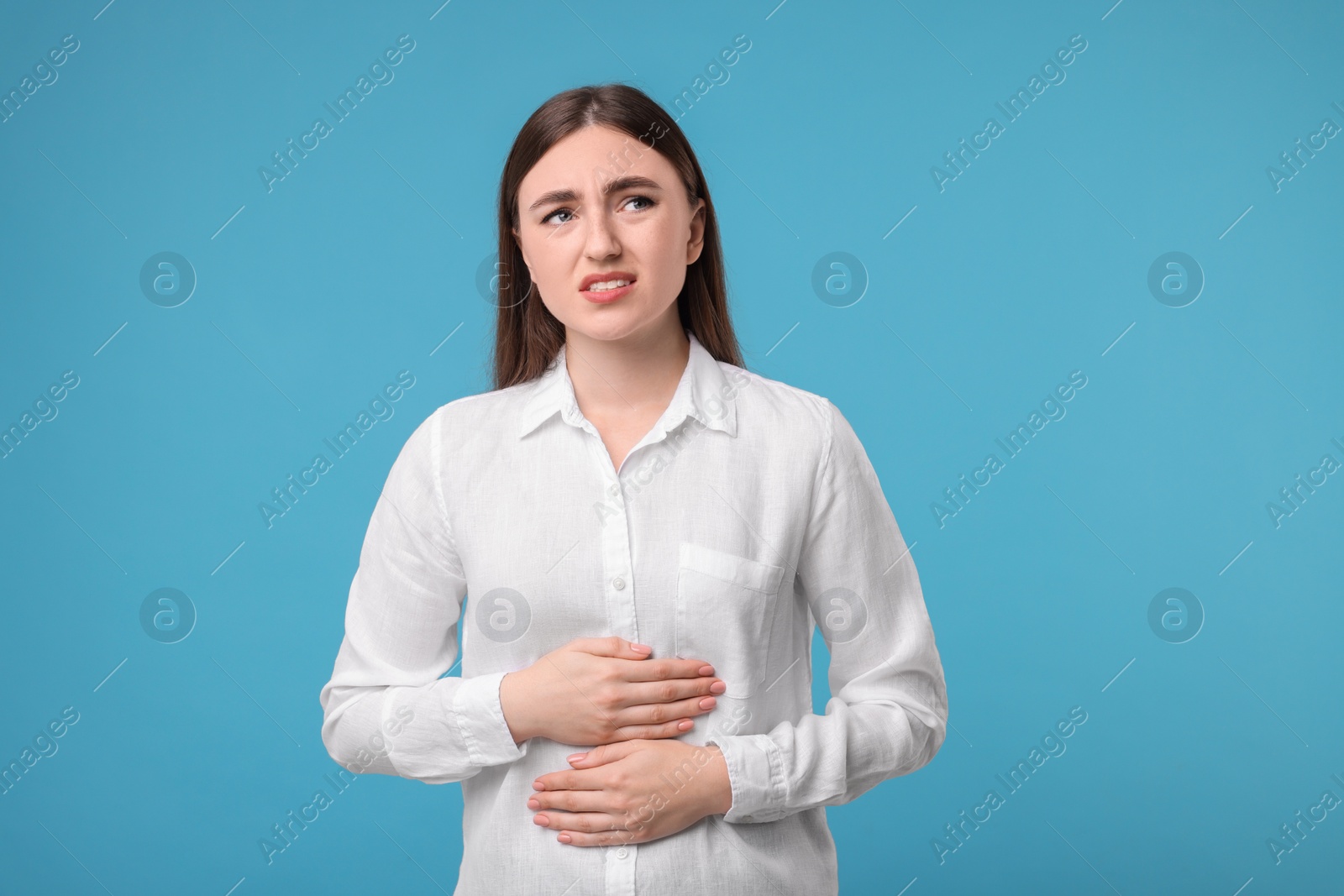 Photo of Young woman suffering from stomach pain on light blue background
