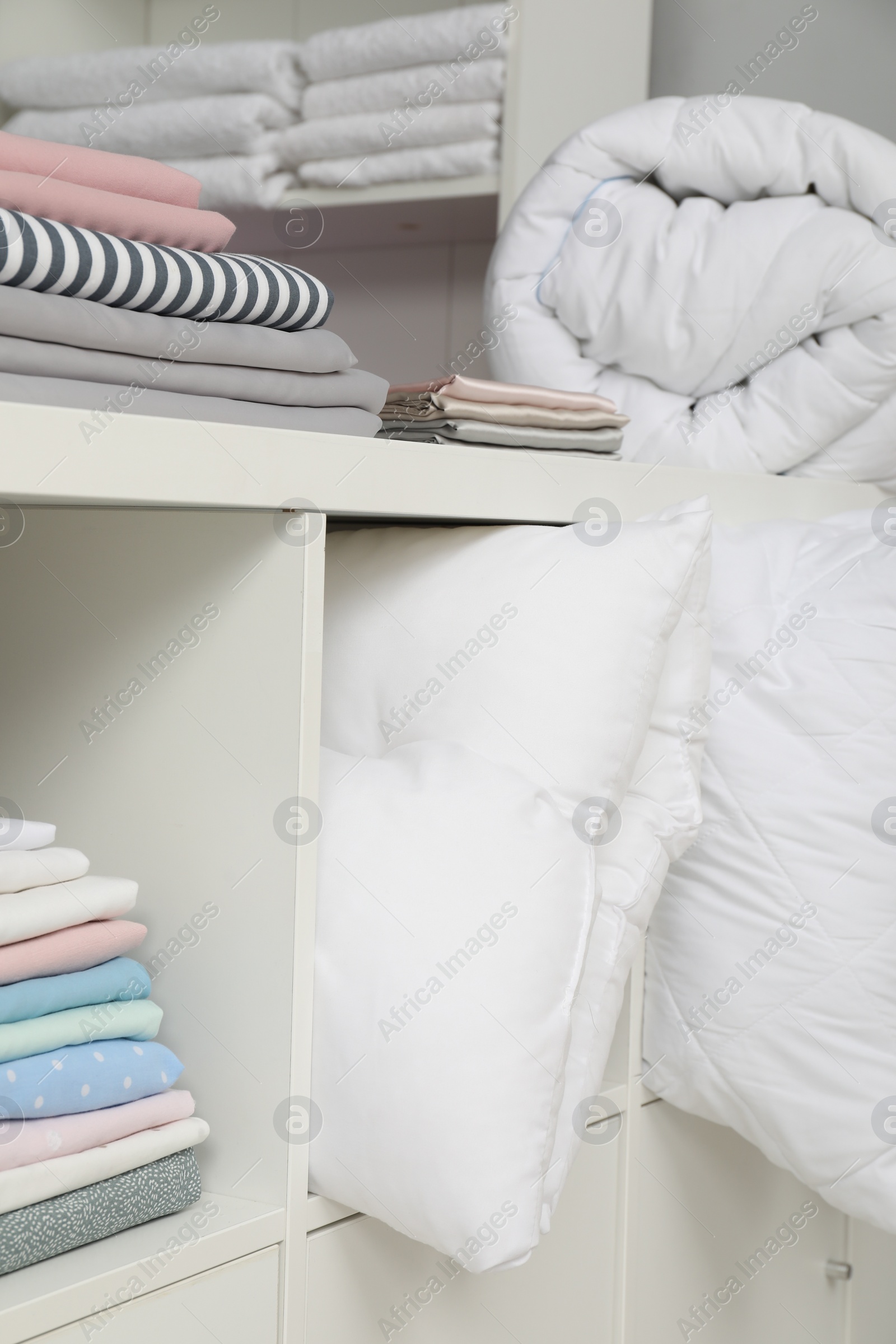 Photo of Different colorful bed linens and pillows on shelves in home textiles store