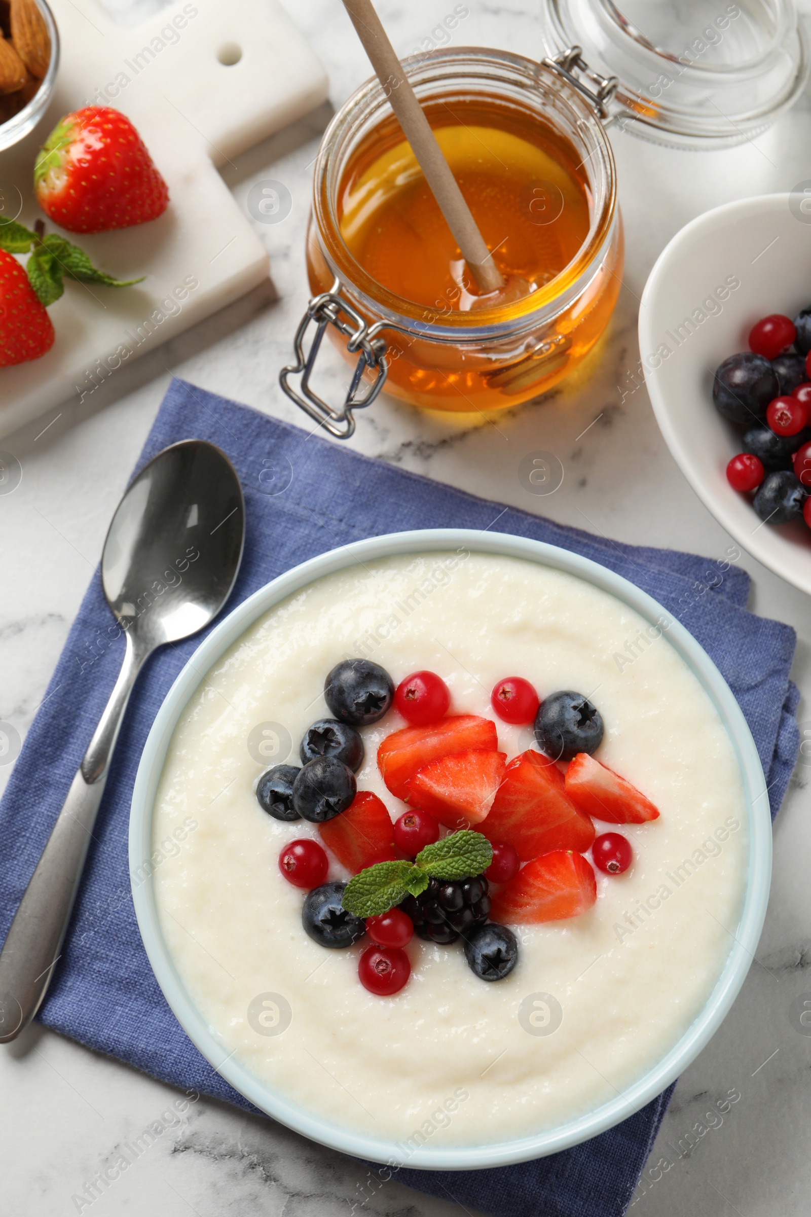 Photo of Delicious semolina pudding with berries on white marble table, flat lay