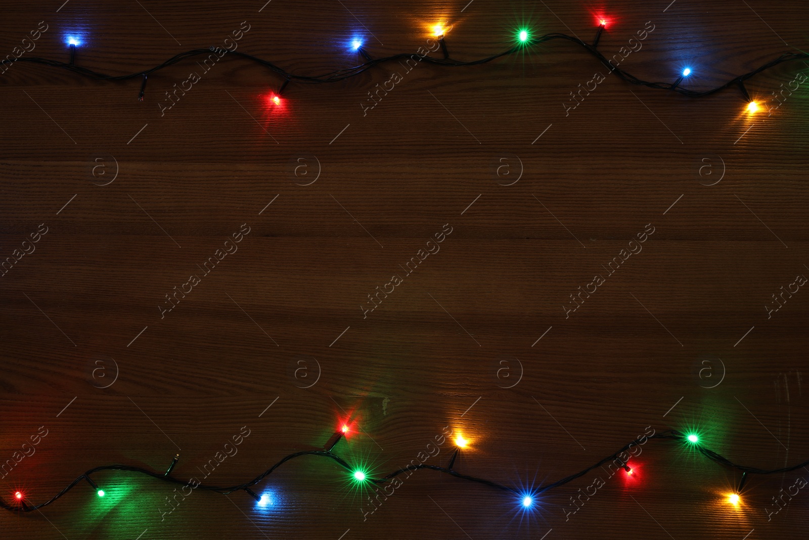 Photo of Frame of colorful Christmas lights on wooden table, top view. Space for text