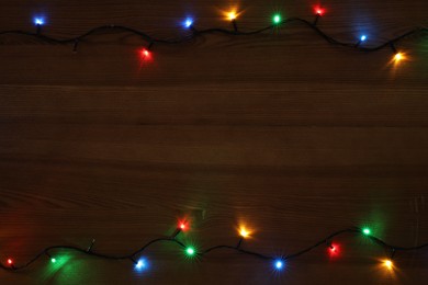Photo of Frame of colorful Christmas lights on wooden table, top view. Space for text