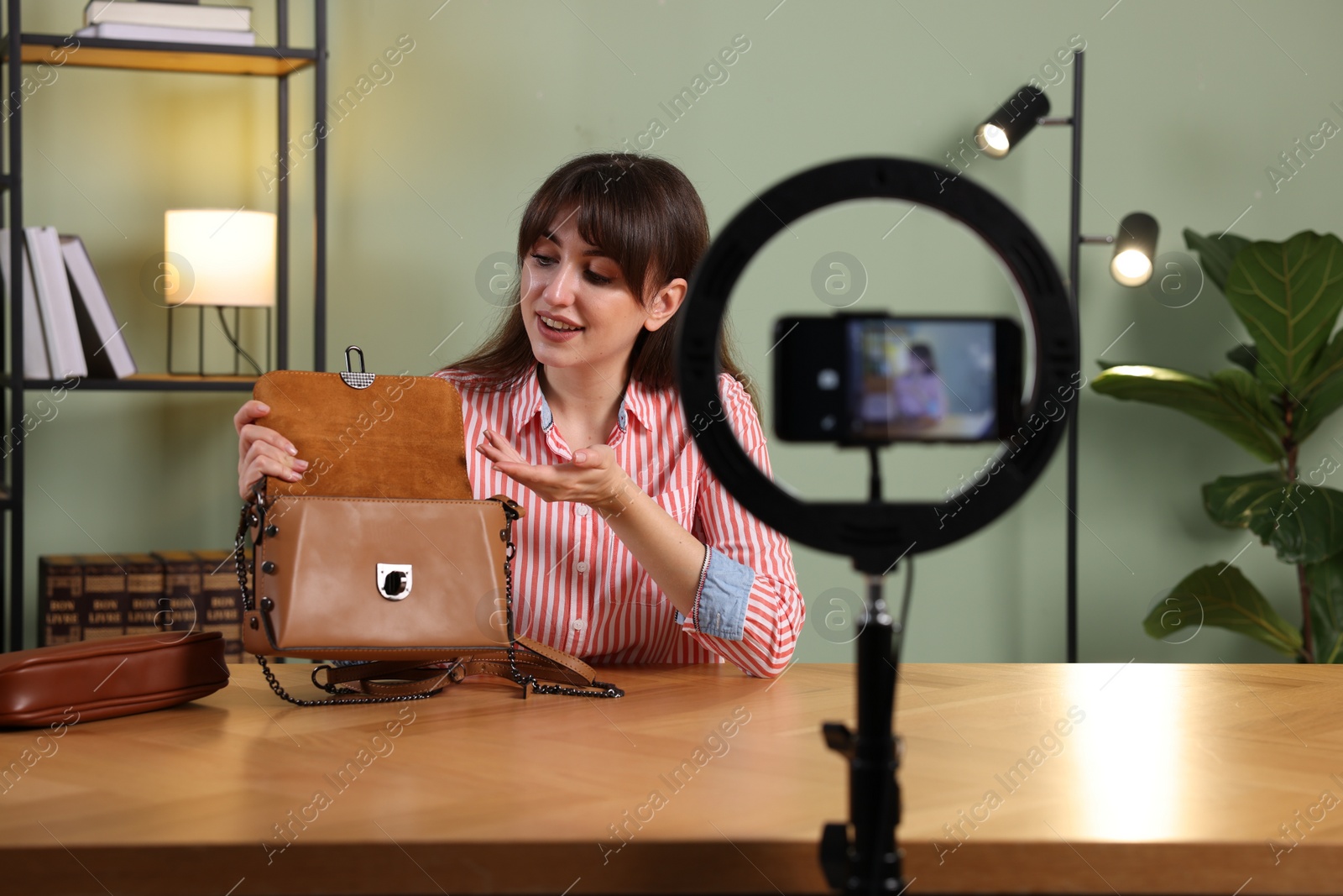 Photo of Smiling fashion blogger recording video while showing bag at home