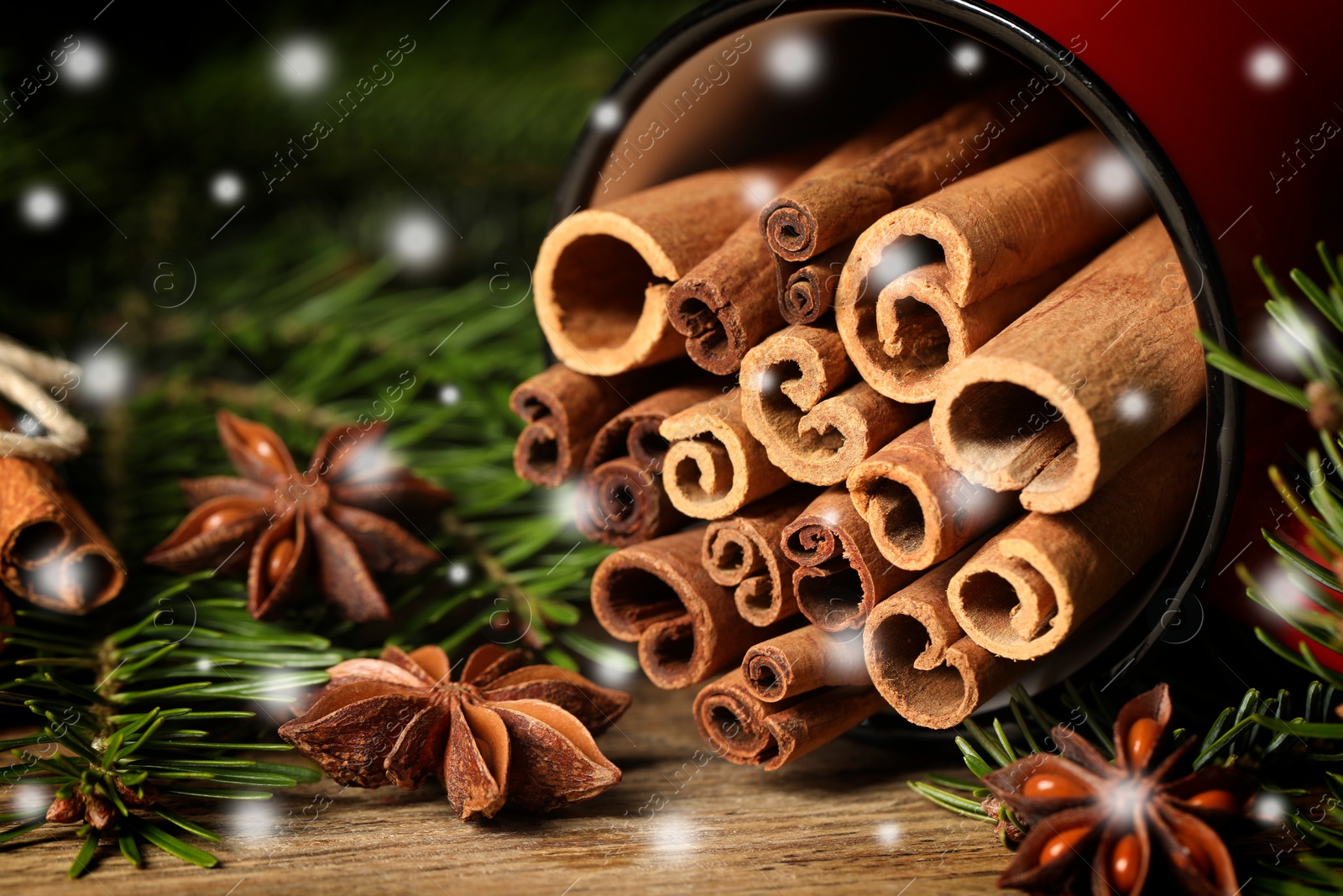 Image of Cinnamon in red mug and anise surrounded by fir tree branches on wooden table, closeup