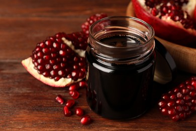 Photo of Glass jar of tasty pomegranate sauce and fresh ripe fruit on wooden table