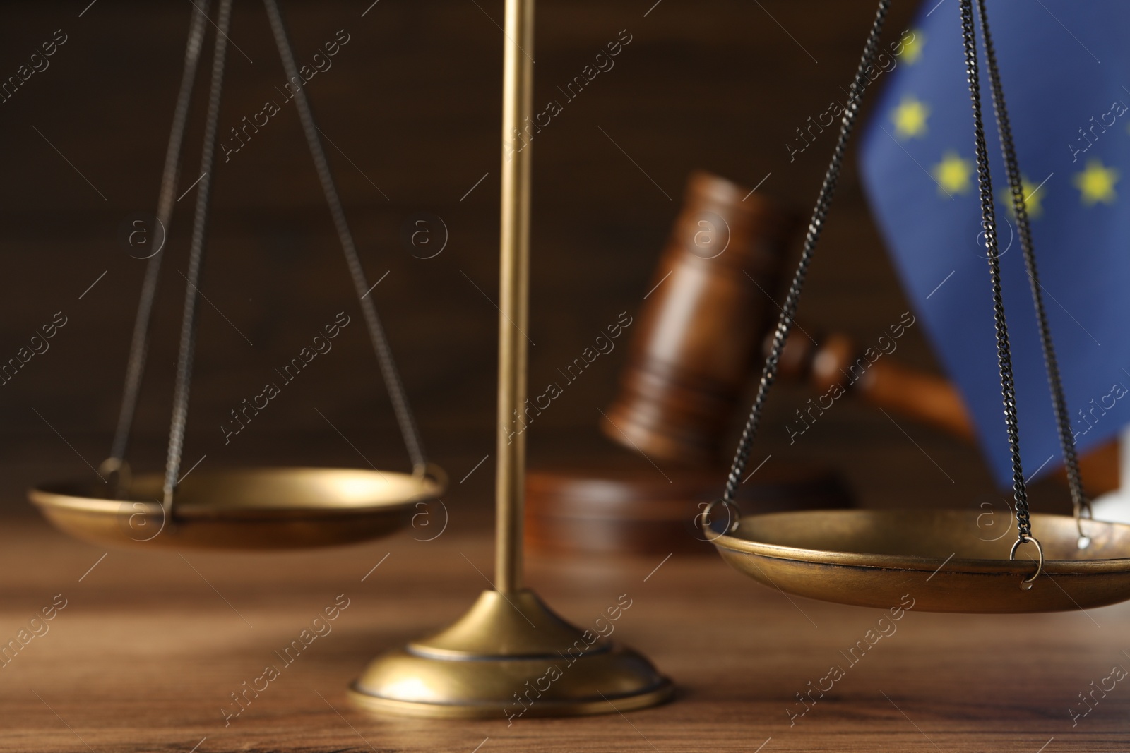 Photo of Scales of justice, judge's gavel and European Union flag on wooden table, closeup