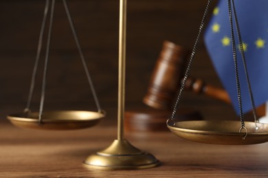 Scales of justice, judge's gavel and European Union flag on wooden table, closeup