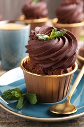 Delicious chocolate cupcake with mint on wooden table, closeup