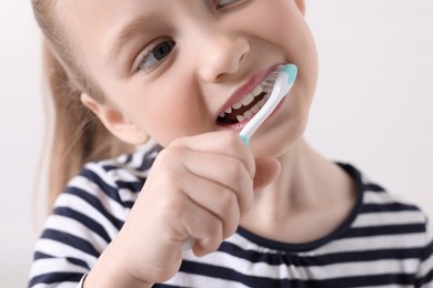 Photo of Little girl brushing her teeth with plastic toothbrush on white background, closeup