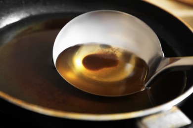 Photo of Frying pan and ladle with used cooking oil on stove, closeup