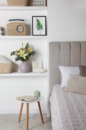 Stylish vase with flowers, retro radio and decor on shelves indoors. Bedroom interior elements