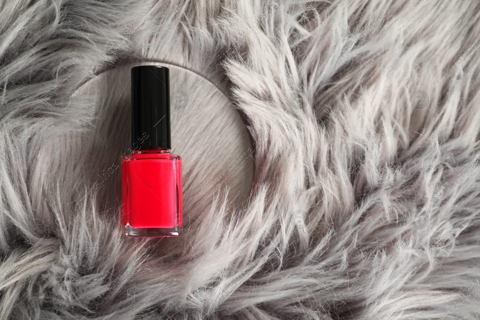 Photo of Bright nail polish in bottle on grey faux fur, top view. Space for text