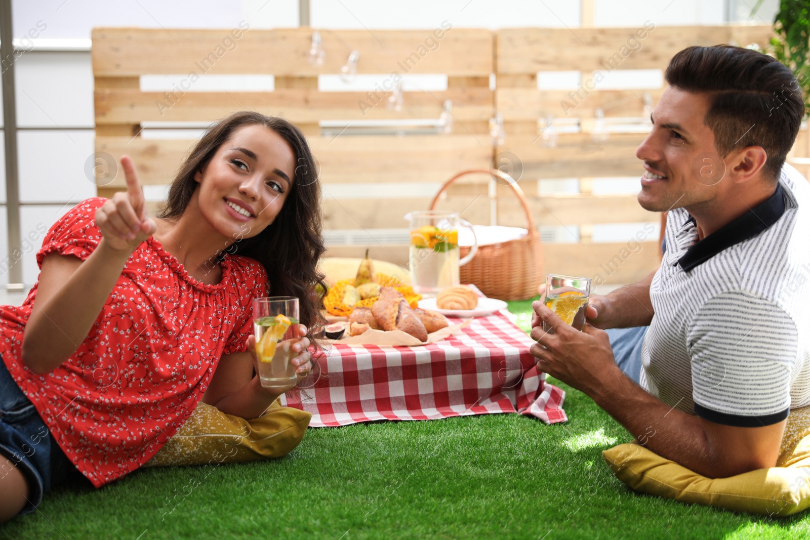 Photo of Happy couple with refreshing drinks imitating picnic at home