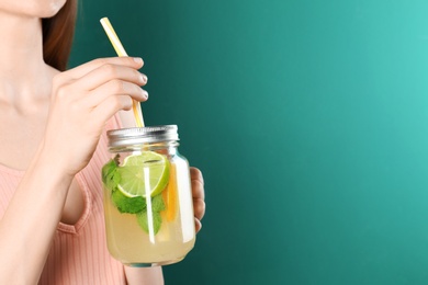 Photo of Woman with Mason jar of natural detox lemonade on green background, closeup. Space for text