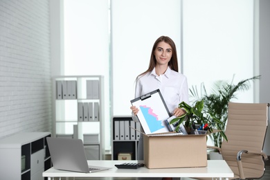 Happy young woman packing stuff in box at office