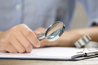 Photo of Woman using magnifying glass at table, closeup