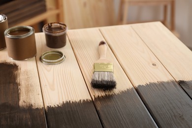 Brush and cans with wood stain on wooden table indoors