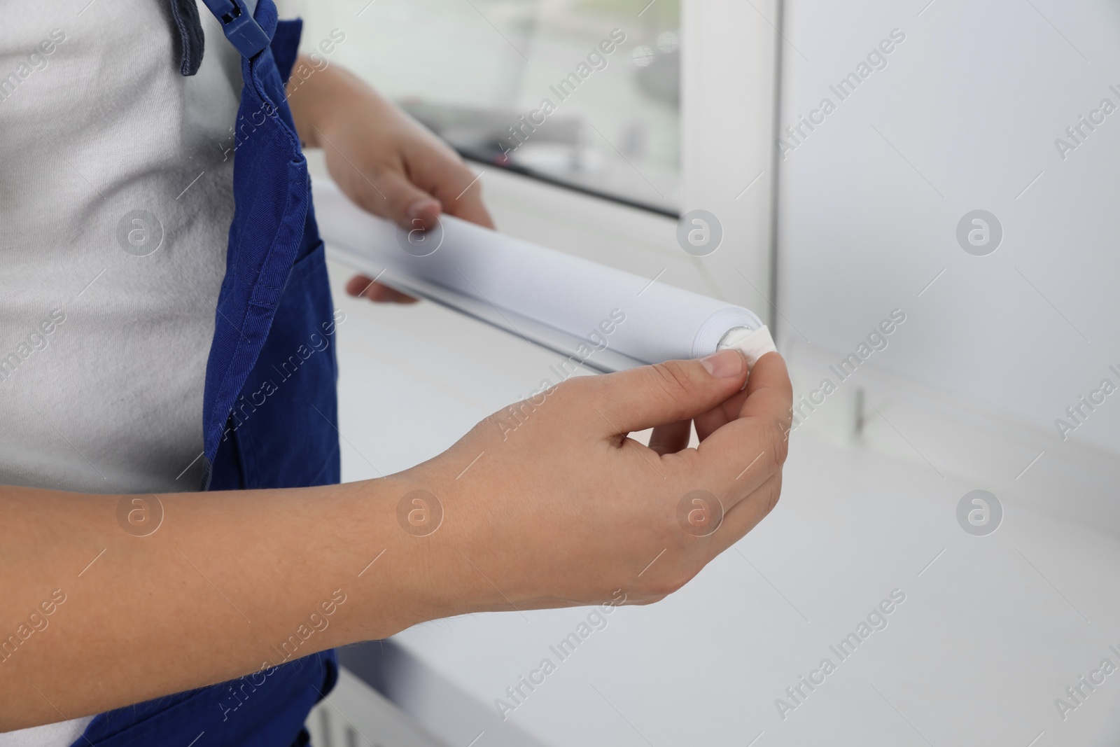 Photo of Worker in uniform installing roller window blind indoors, closeup