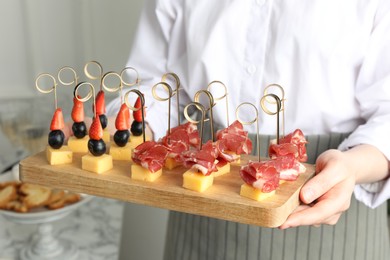 Photo of Woman holding tray of different tasty canapes indoors, closeup