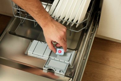 Man putting detergent tablet into open dishwasher indoors, closeup