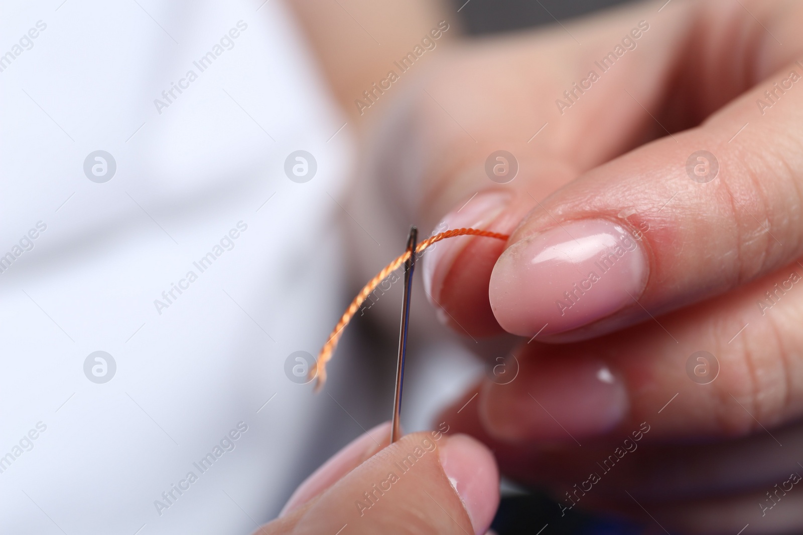 Photo of Woman inserting thread through eye of needle on blurred background, closeup