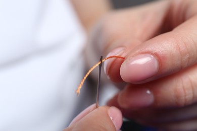 Photo of Woman inserting thread through eye of needle on blurred background, closeup