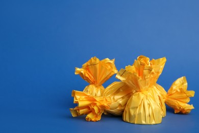 Photo of Candies in yellow wrappers on blue background. Space for text