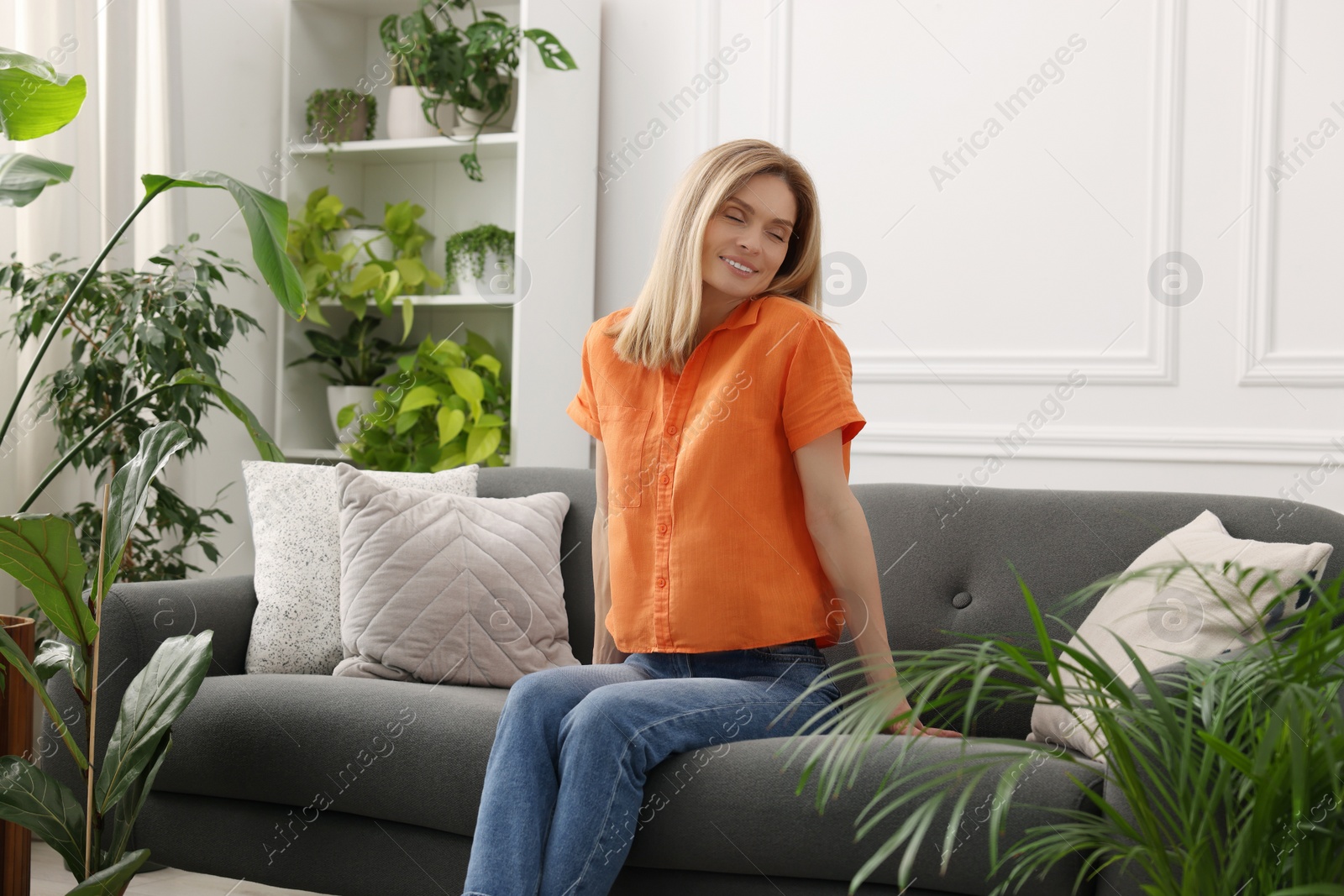 Photo of Woman sitting on sofa surrounded by beautiful potted houseplants at home