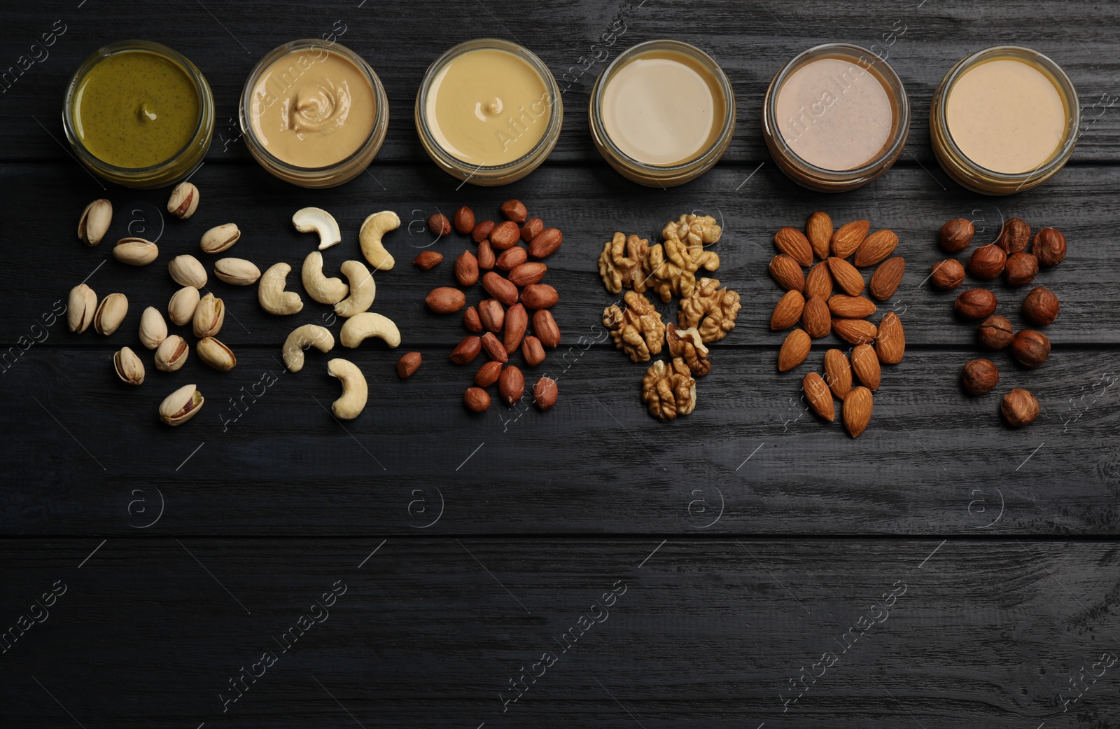 Photo of Jars with butters made of different nuts and ingredients on black wooden table, flat lay. Space for text