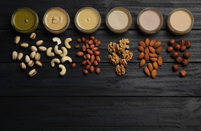 Photo of Jars with butters made of different nuts and ingredients on black wooden table, flat lay. Space for text