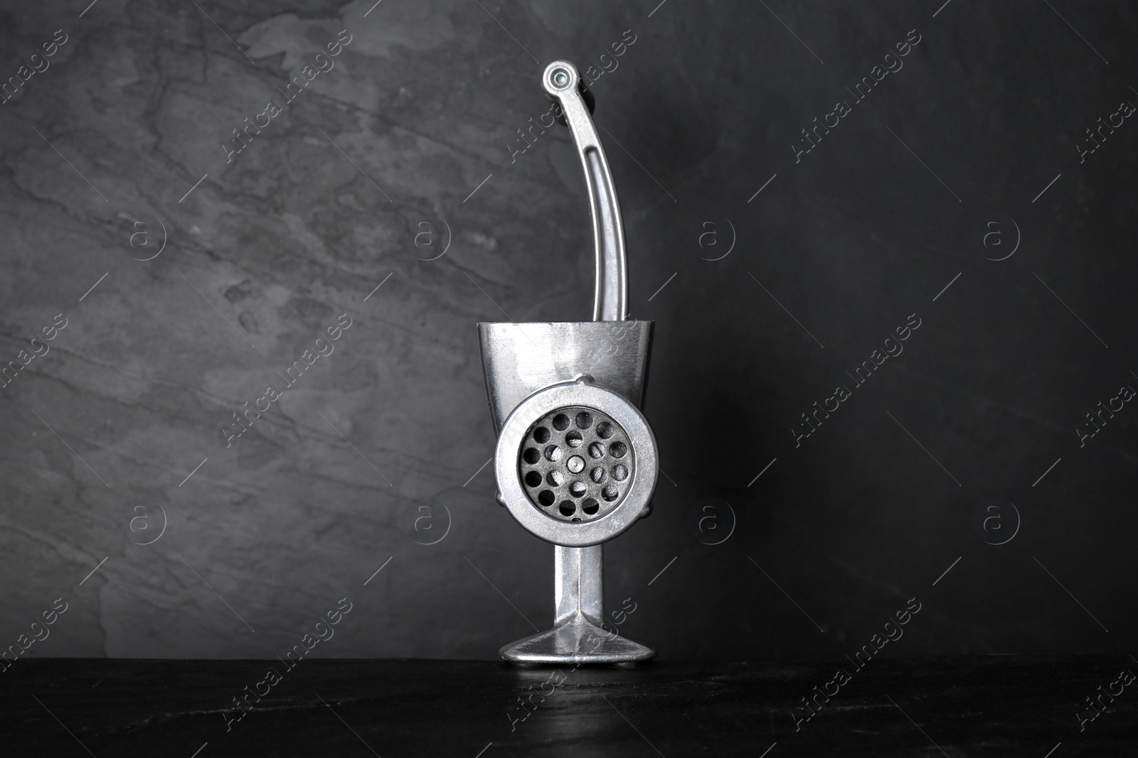 Photo of Metal manual meat grinder on dark table against black background