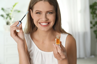 Photo of Young woman applying oil on her eyelashes at home