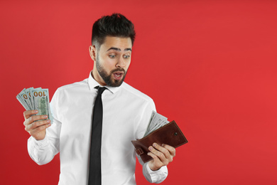 Photo of Emotional young man with money and wallet on crimson background. Space for text
