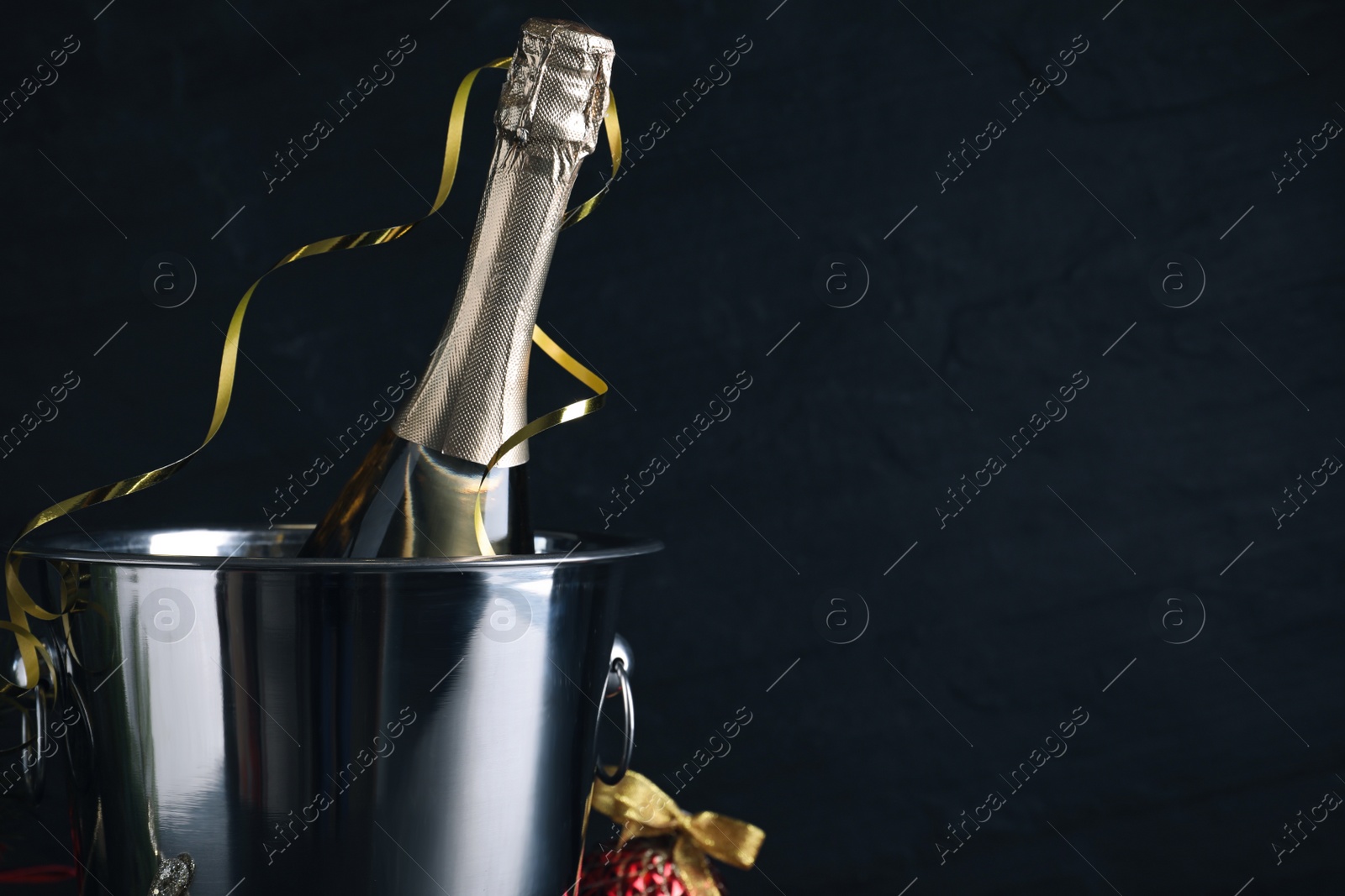 Photo of Happy New Year! Bottle of sparkling wine in bucket on black background, space for text