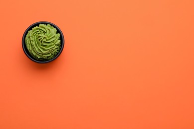 Photo of Bowl with swirl of wasabi paste on orange background, top view. Space for text