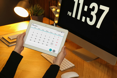 Photo of Woman using tablet with calendar app at workplace, closeup