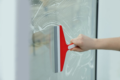 Photo of Woman cleaning window with squeegee indoors, closeup