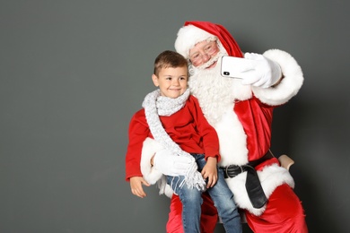 Photo of Authentic Santa Claus taking selfie with little boy on grey background