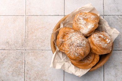 Photo of Delicious profiteroles with powdered sugar on white tiled table, top view. Space for text