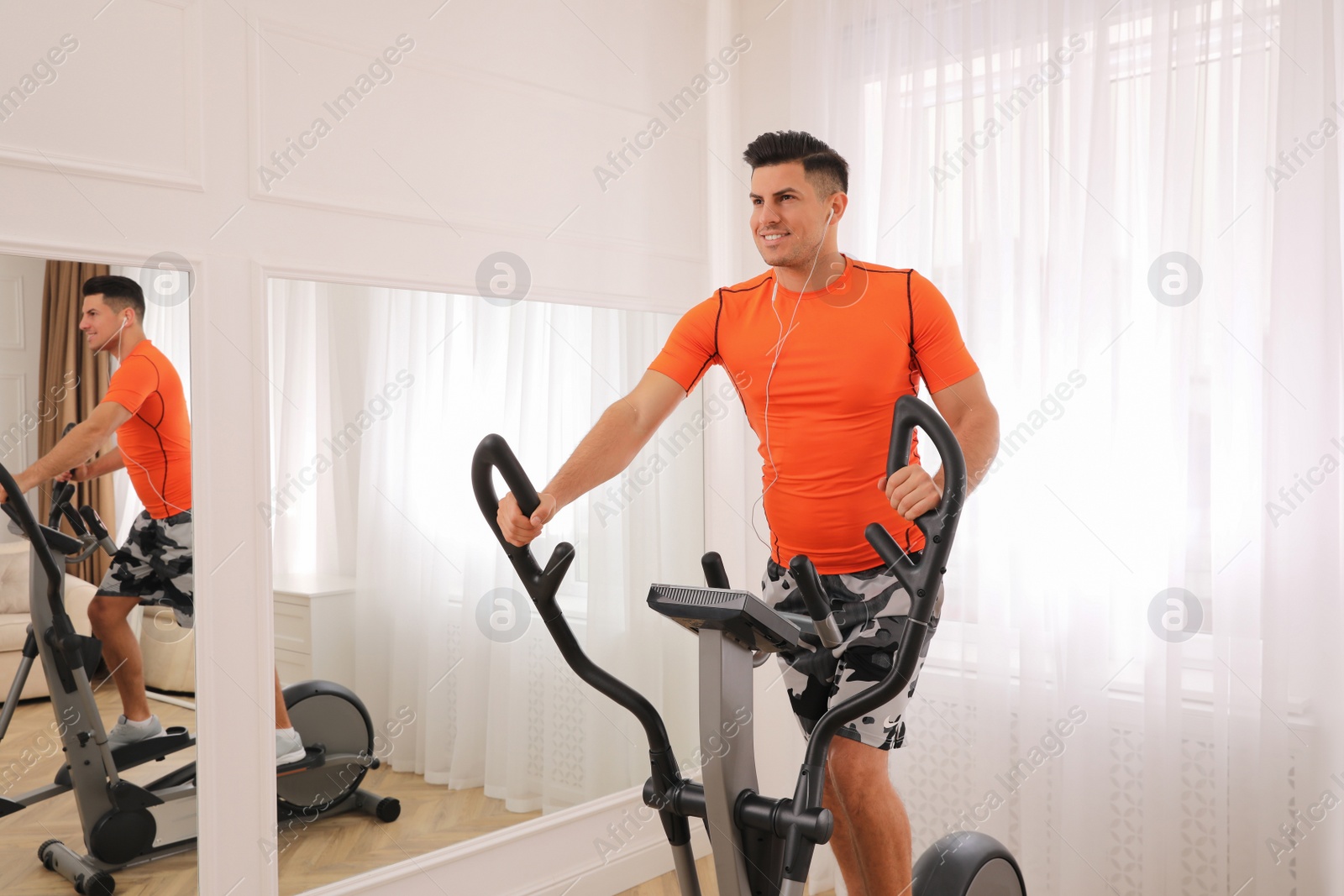 Photo of Man using modern elliptical machine at home