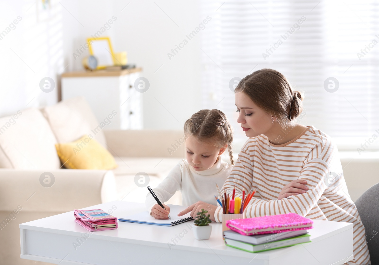 Photo of Woman helping her daughter with homework at table indoors