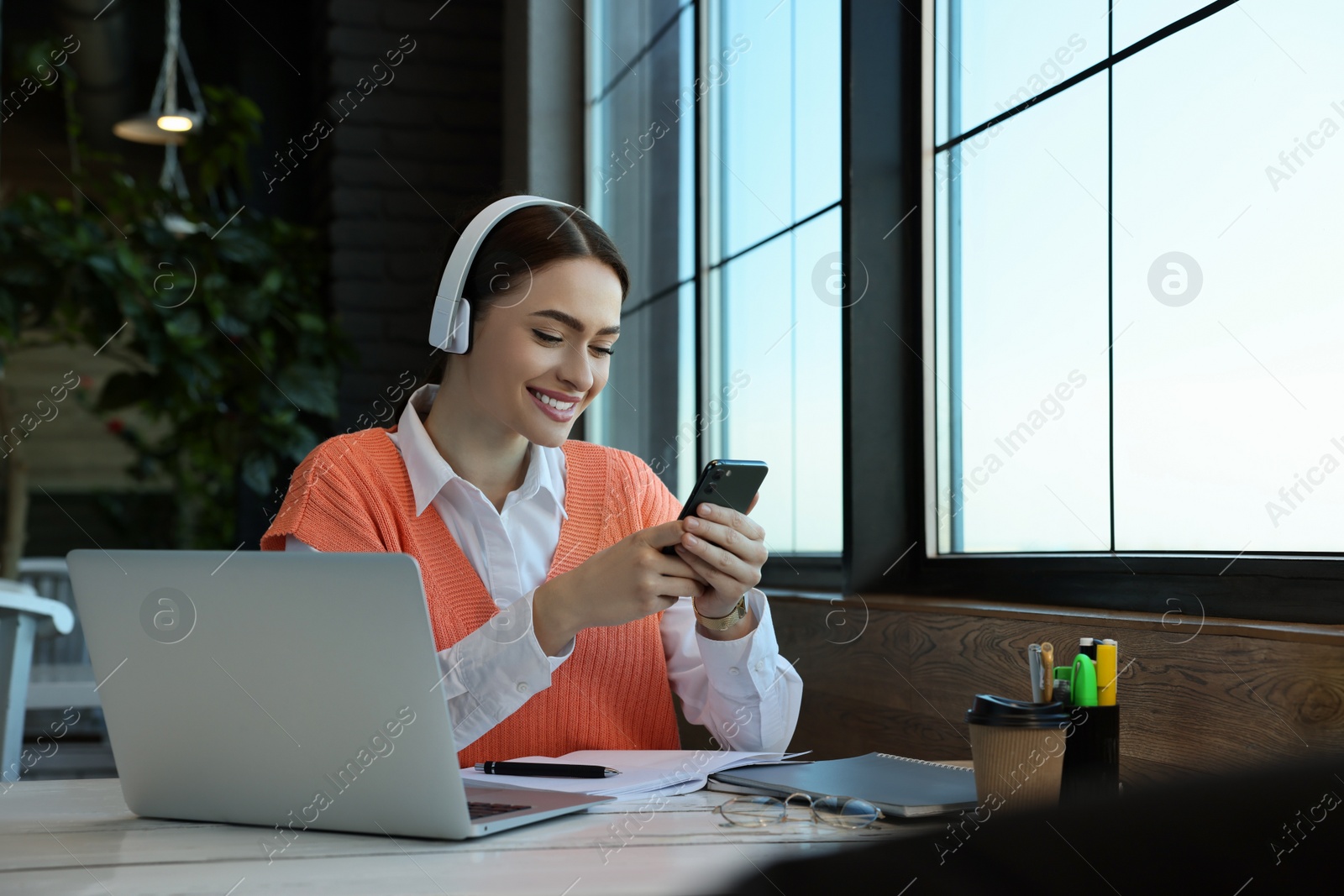 Photo of Young female student with laptop using smartphone while studying at table in cafe