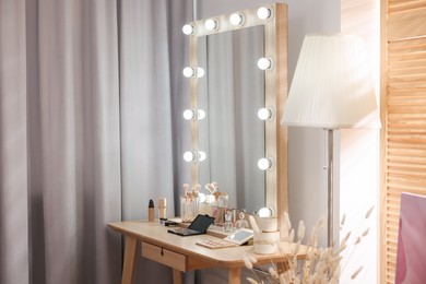Photo of Makeup room. Stylish mirror and different beauty products on wooden dressing table indoors