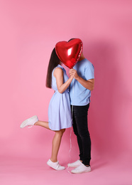 Photo of Lovely couple hiding behind heart shaped balloon on pink background. Valentine's day celebration