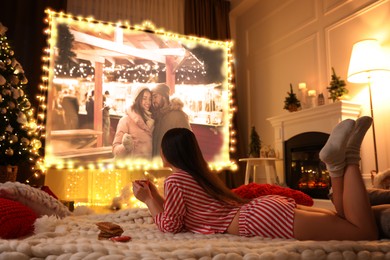 Woman watching romantic Christmas movie via video projector in room. Cozy winter holidays atmosphere