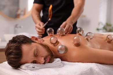 Therapist giving fire cupping treatment to patient on massage couch in spa salon