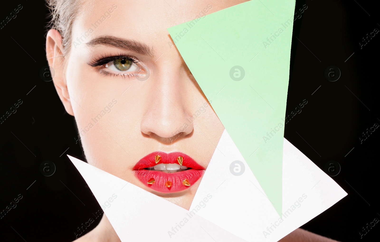 Photo of Beautiful young model with decorative spikes on lips and paper against black background