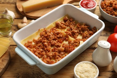 Photo of Cooking lasagna. Pasta sheets and minced meat in baking tray on wooden table, closeup