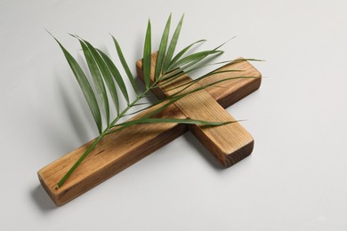 Photo of Wooden cross and palm leaf on light grey background. Easter attributes