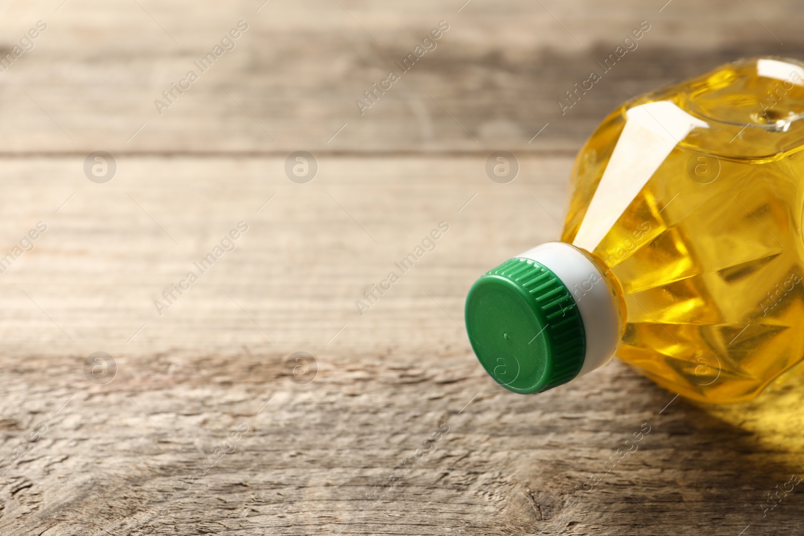 Photo of Plastic bottle of cooking oil on wooden table. Space for text